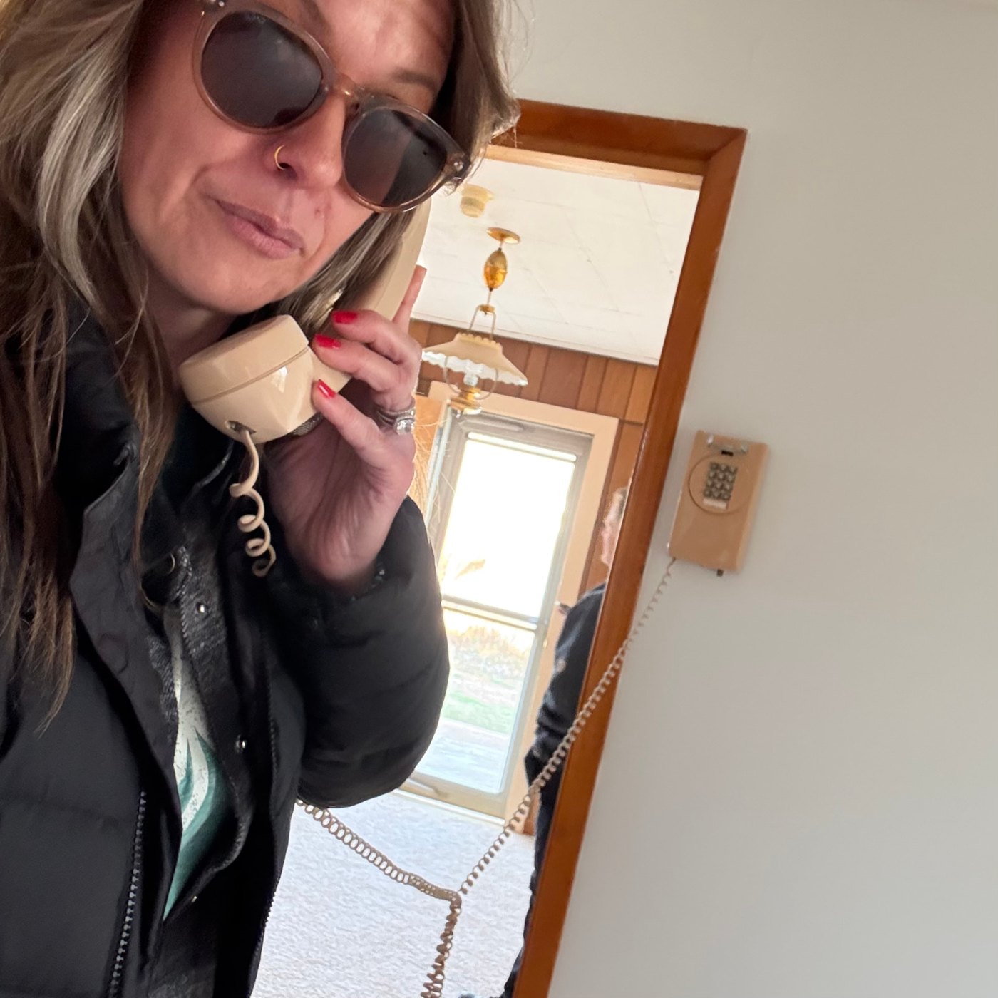 Christin Mack holding the handset of a vintage beige wall telephone